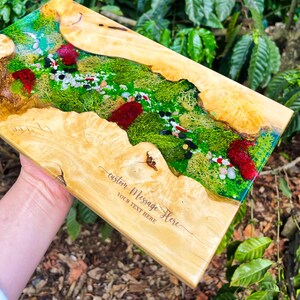May include: A rectangular wooden serving board with a river scene design. The river features green moss, small stones, and red accents, encased in clear resin. The board has the text "custom Message Here" and "YOUR TEXT HERE" engraved on the wood.