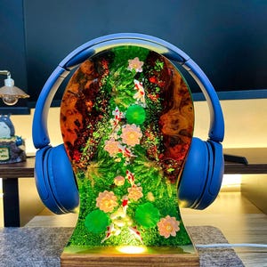 May include: A unique lamp featuring a resin design with a miniature koi pond scene, complete with fish and flowers. The lamp is adorned with blue headphones and sits on a wooden base. The pond scene is illuminated from within.