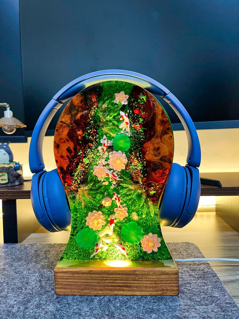 May include: A unique lamp featuring a resin design with a miniature koi pond scene, complete with fish and flowers. The lamp is adorned with blue headphones and sits on a wooden base. The pond scene is illuminated from within.