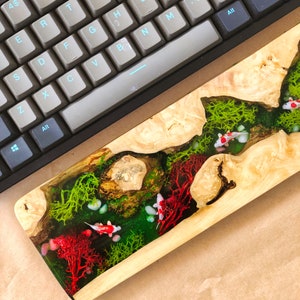 May include: A wooden keyboard wrist rest with a clear resin inlay featuring red coral, green moss, and white fish.