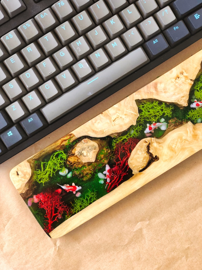 May include: A wooden keyboard wrist rest with a clear resin inlay featuring red coral, green moss, and white fish.