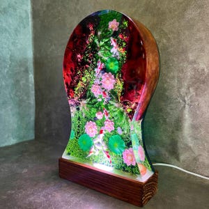 May include: A decorative lamp featuring a resin design with a koi pond scene. The lamp has a wooden base and a curved, clear resin body. The interior showcases pink flowers, green lily pads, and koi fish. The lamp is lit from within.