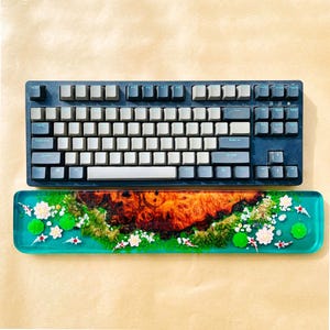 May include: A mechanical keyboard with gray keycaps and a dark blue frame sits above a matching wrist rest. The wrist rest features a vibrant design with a wood grain center, koi fish, white flowers, and green lily pads.