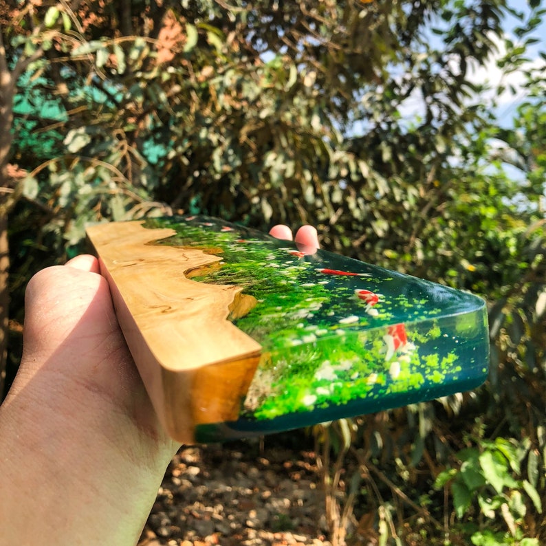 May include: A wooden and resin tray with a green and blue epoxy resin design. The resin has a glittery finish and features red and white fish shapes.