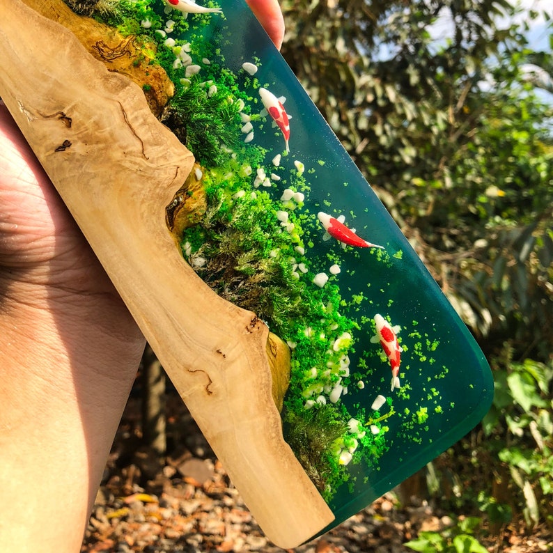 May include: A resin art piece with a wood base and a green epoxy resin section. The resin section features white and green glitter and three red and white koi fish.