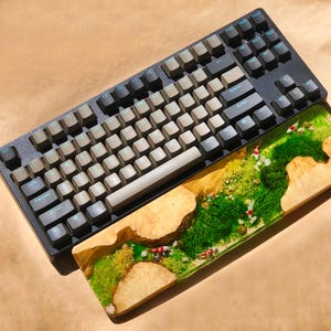 Puede incluir: Un teclado mec&aacute;nico gris y negro con un juego de teclas grises y un reposamu&ntilde;ecas de madera con un dise&ntilde;o de musgo verde y peces.