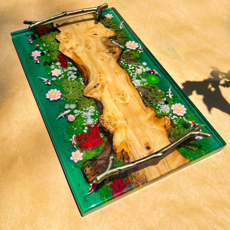 May include: A rectangular serving tray with a vibrant green resin base, featuring a natural wood centerpiece. The tray is adorned with miniature koi fish, flowers, moss, and decorative handles. The tray measures approximately 12 inches long and 8 inches wide.