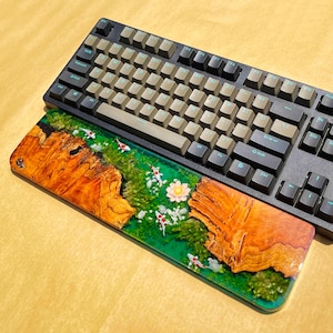 May include: A black mechanical keyboard with tan keycaps and a custom resin wrist rest. The wrist rest features a vibrant design of a koi pond with orange and white fish, green foliage, and a flower.