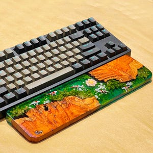 May include: A black mechanical keyboard with gray keycaps rests above a custom wrist rest. The wrist rest features a vibrant design with a wood grain pattern, green resin, and miniature koi fish, creating a unique and artistic aesthetic.