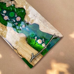 May include: A decorative wooden serving tray with a river scene. The tray features a clear epoxy river with koi fish, lily pads, and flowers. The tray has a natural wood edge and a metal branch handle.