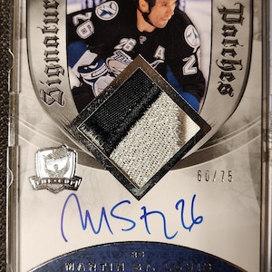 May include: A hockey card featuring a player in a blue and white jersey with a black and white jersey patch. The card is numbered 60/75 and has the player's signature.