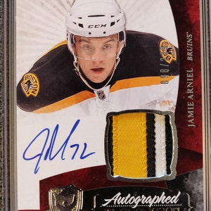 May include: A hockey card featuring Jamie Arniel of the Boston Bruins. The card is a rookie card and is autographed. The card is in a protective case.