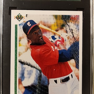 Puede incluir: Una tarjeta de béisbol Upper Deck SP1 de 1991 con Michael Jordan en un uniforme de béisbol rojo y blanco, sosteniendo un bate y usando una gorra blanca con un logotipo rojo. La tarjeta está calificada con 96 por SGC.