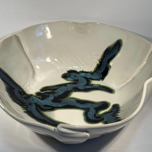May include: A large white ceramic bowl with a wavy rim. The bowl has a blue and green abstract design with a speckled texture.