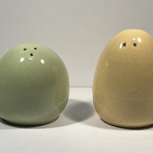 May include: A set of two ceramic salt and pepper shakers shaped like eggs. The salt shaker is green and the pepper shaker is yellow.