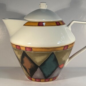 May include: A white ceramic teapot with a geometric pattern in shades of brown, red, green, and grey. The teapot has a lid and a handle.