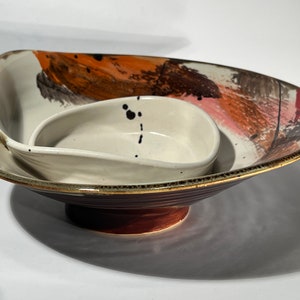 May include: A set of two ceramic bowls, one nested inside the other. The larger bowl has a brown, orange, and pink abstract design. The smaller bowl is white with black speckles.
