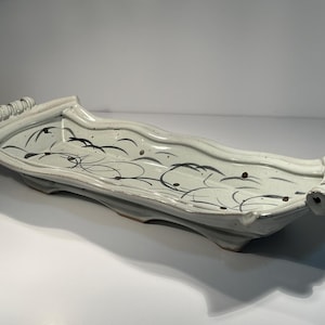 May include: A ceramic serving tray with a light blue glaze and black abstract design. The tray has a wavy shape with rolled handles on each end. The design includes black lines and dots.