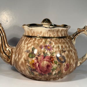 May include: A brown and white teapot with a floral pattern and gold trim. The teapot has a lid with a gold knob.