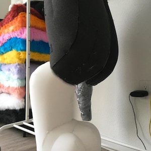 May include: A foam costume base featuring a large black upper torso section and a white lower leg and foot section. The black foam is shaped with seams, while the white foam forms a rounded, digit-like foot structure with a silver duct-taped limb.