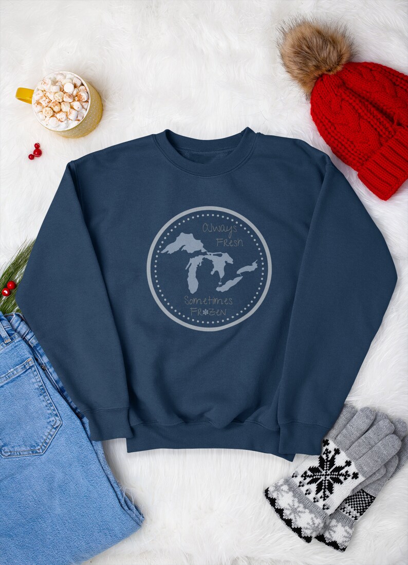 May include: A navy blue sweatshirt with a gray circle graphic featuring a map of the Great Lakes and the text "Always Fresh, Sometimes Frozen".