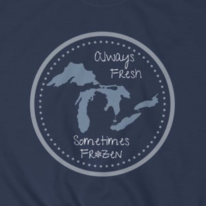 May include: A navy blue t-shirt with a gray circle design featuring a map of the Great Lakes and the text "Always Fresh Sometimes Frozen" with a snowflake.