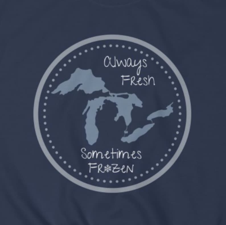 May include: A navy blue t-shirt with a gray circle design featuring a map of the Great Lakes and the text "Always Fresh Sometimes Frozen" with a snowflake.