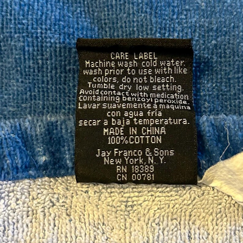 May include: A black care label with white text, including washing instructions and fabric details. The label is on a blue and white textured fabric. The label reads "MADE IN CHINA" and "100% COTTON."