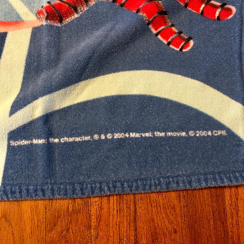 May include: Blue and white Spider-Man beach towel with red detailing. The towel features a design of Spider-Man's web and the text "Spider-Man: the character, &copy; & &copy; 2004 Marvel, the movie, &copy; 2004 CPIL."
