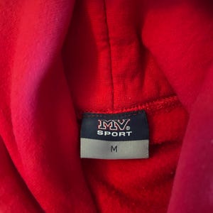 Puede incluir: Una sudadera con capucha de color rojo brillante que presenta una etiqueta rectangular en el cuello interior. La etiqueta tiene un fondo azul oscuro con el texto blanco MV SPORT y una secci&oacute;n inferior gris con la talla M en letras negras.