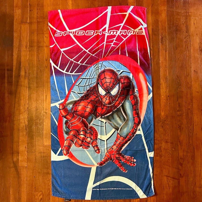 May include: A rectangular beach towel featuring Spider-Man in a dynamic pose, set against a web design and a blue and red background. The words "SPIDER-MAN 2" are printed at the top.