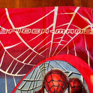 May include: Red Spider-Man beach towel with white web design and the text "SPIDER-MAN". The bottom of the towel features a close-up of Spider-Man's face with a webbed mask.