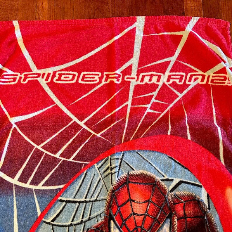 May include: Red Spider-Man beach towel with white web design and the text "SPIDER-MAN". The bottom of the towel features a close-up of Spider-Man's face with a webbed mask.