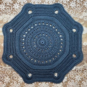 May include: A dark blue, handmade crochet doily in an octagonal shape. The doily has a central spiral design, surrounded by concentric circles and decorative holes. The textured yarn gives a detailed, handcrafted appearance, suitable for home decor.