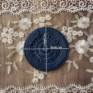 Puede incluir: Un posavasos circular azul marino, de 12,7 cm de di&aacute;metro, hecho de un material tejido apretado. El posavasos est&aacute; centrado en un fondo de encaje bordado con motivos florales.