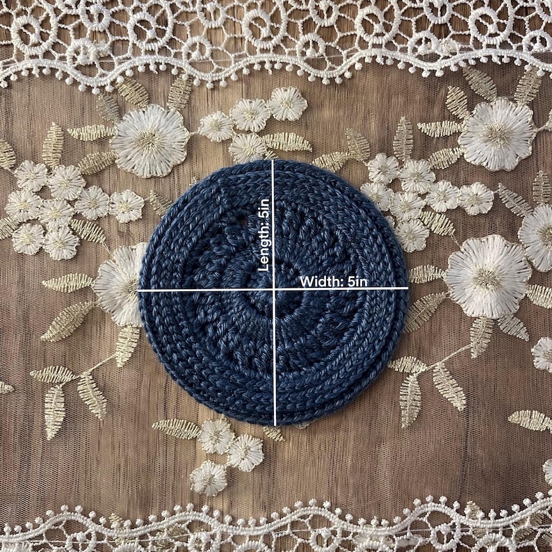 Puede incluir: Un posavasos circular azul marino, de 12,7 cm de di&aacute;metro, hecho de un material tejido apretado. El posavasos est&aacute; centrado en un fondo de encaje bordado con motivos florales.