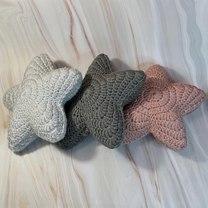 May include: Three crocheted star-shaped cushions in grey, dark grey, and pink.