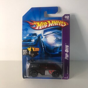 May include: A black Hot Wheels toy car with a red stripe and the number 7 on the side. The car is in a plastic package with a blue background and the words "Hot Wheels" and "Pop-Offs" printed on it. The car is part of a series of 4 and is number 2 of 4.