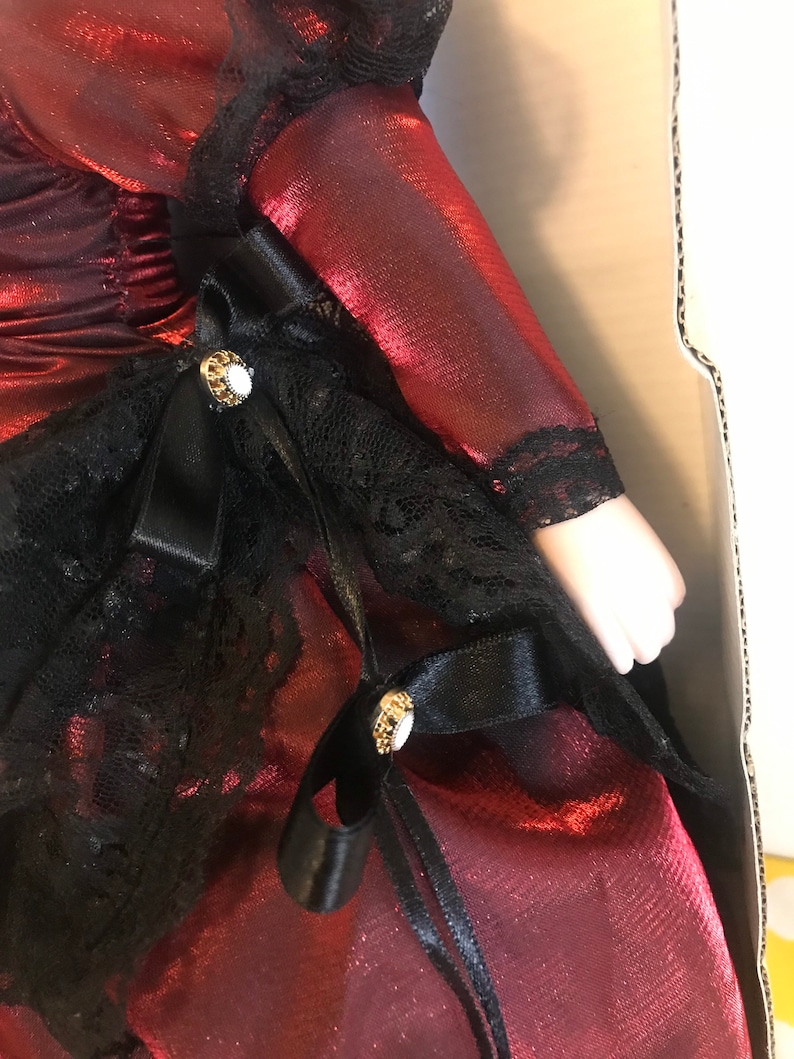 May include: A red satin dress with black lace trim and black satin ribbon bows. The dress has gold-colored buttons with white stones.