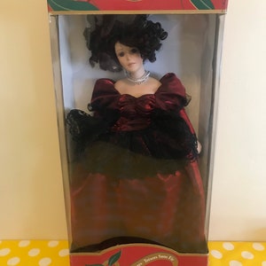 May include: A porcelain doll in a red and black dress with a black hat. The doll is in a box with the text "Timeless Treasures Tr&eacute;sors Sans Fir" and "Genuine 18" Porcelain Doll Poup&eacute;e de Porcelaine V&eacute;ritable 18 po".