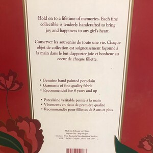 May include: Back of a box for a collectible doll. The box is red with a floral design. The text on the box reads "Hold on to a lifetime of memories. Each fine collectible is tenderly handcrafted to bring joy and happiness to any girl's heart." The box also includes a list of features, including "Genuine hand painted porcelain", "Garments of fine quality fabric", and "Recommended for 8 years and up".