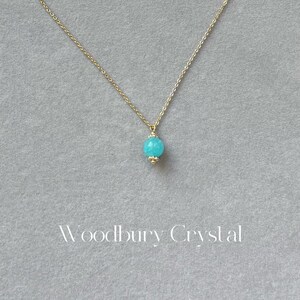 May include: A delicate gold chain necklace with a single, round turquoise gemstone pendant.