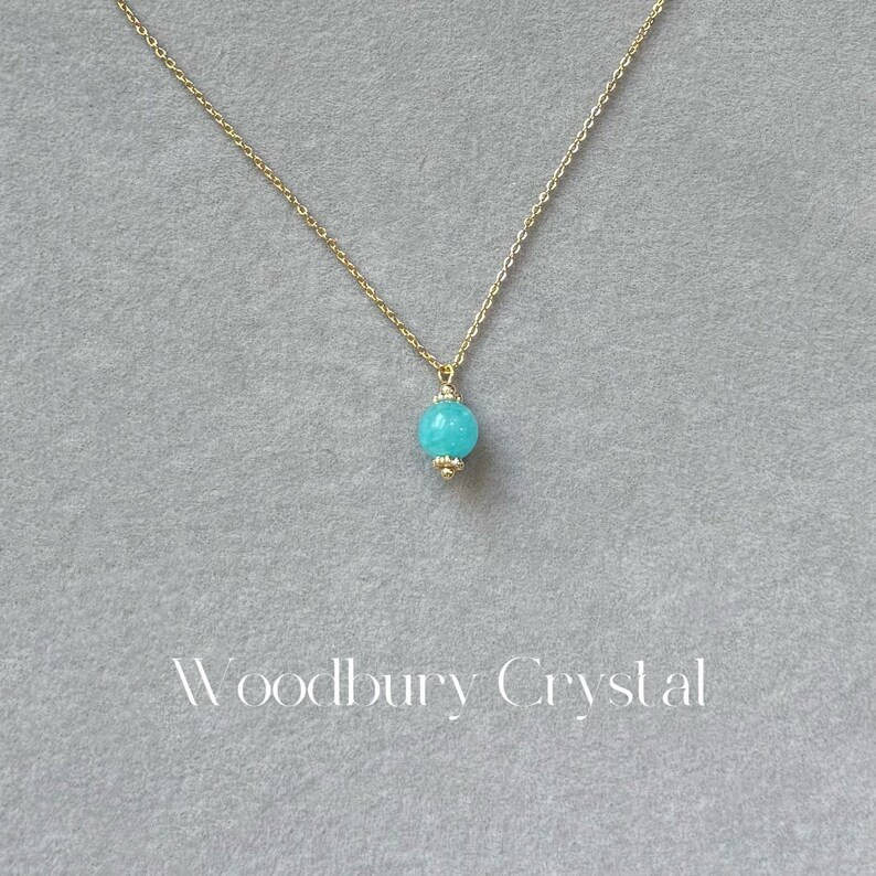 May include: A delicate gold chain necklace with a single, round turquoise gemstone pendant.