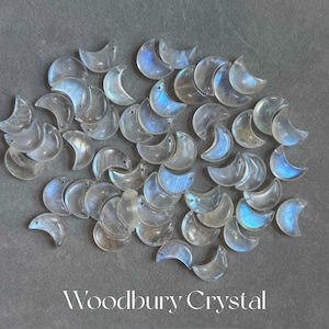 May include: A collection of iridescent moonstone crescent charms, each with a unique shimmer and a smooth, polished finish. The charms are arranged in a random pattern on a gray background.