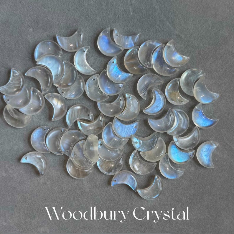 May include: A collection of iridescent moonstone crescent charms, each with a unique shimmer and a smooth, polished finish. The charms are arranged in a random pattern on a gray background.