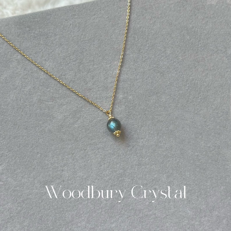 May include: A gold chain necklace with a dark blue oval pendant. The pendant has a subtle shimmer.