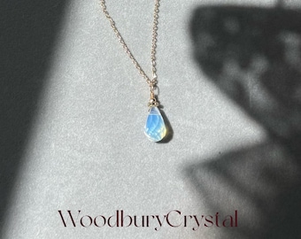 May include: A delicate gold chain necklace with a teardrop-shaped opal pendant. The opal is iridescent with shades of blue and white.