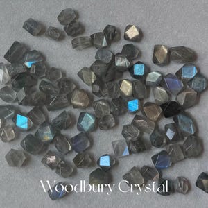 May include: A collection of gray labradorite gemstone beads, each cut into a faceted, geometric shape. The beads have a iridescent sheen, with flashes of blue and green.