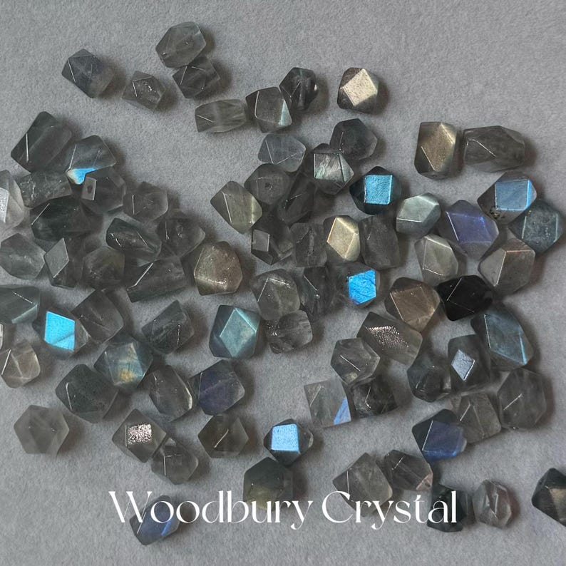 May include: A collection of gray labradorite gemstone beads, each cut into a faceted, geometric shape. The beads have a iridescent sheen, with flashes of blue and green.