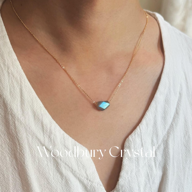 May include: A gold chain necklace with a blue iridescent labradorite gemstone pendant.